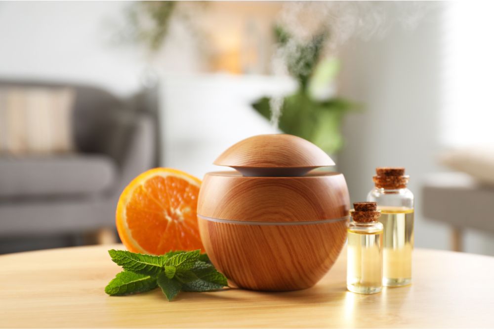 Diffuseur d’arômes en bois avec des huiles essentielles, de la menthe et de l’orange dans un intérieur douillet.