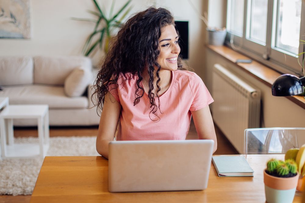 Femme souriante devant un ordinateur portable dans un bureau à domicile, symbole de bien-être grâce à l'aromathérapie au travail