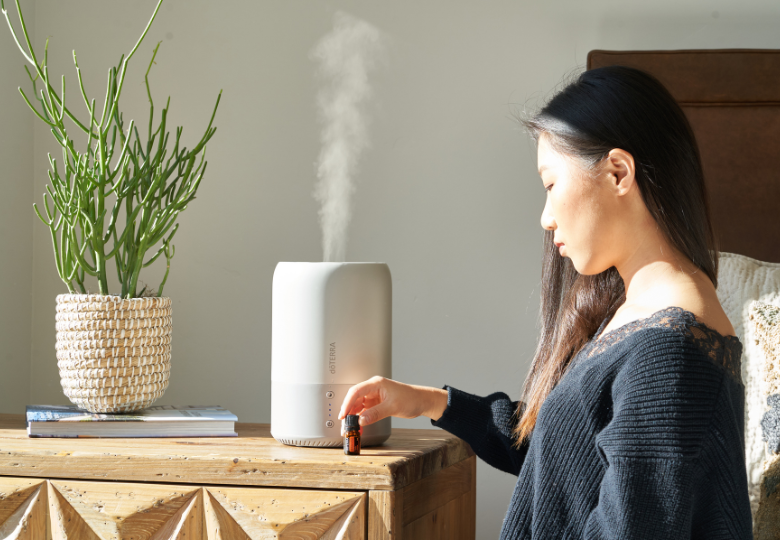 Une femme verse de l'huile essentielle dans un diffuseur d'arômes pour préparer une soirée paisible.